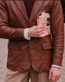 Modello che tiene un giornale e cammina per strada con una giacca di pelle marrone da uomo di Cycas d'Or.