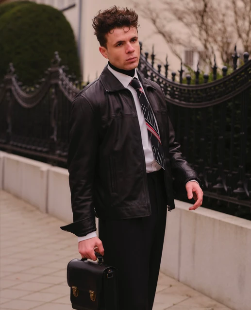 Uomo che tiene una valigia, indossa una giacca di pelle nera Kent di Cycas d'Or in uno stile business casual.