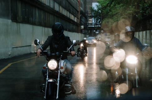 3 motor riders on the road wearing black leather jackets from Cycas d'Or in a rainy day